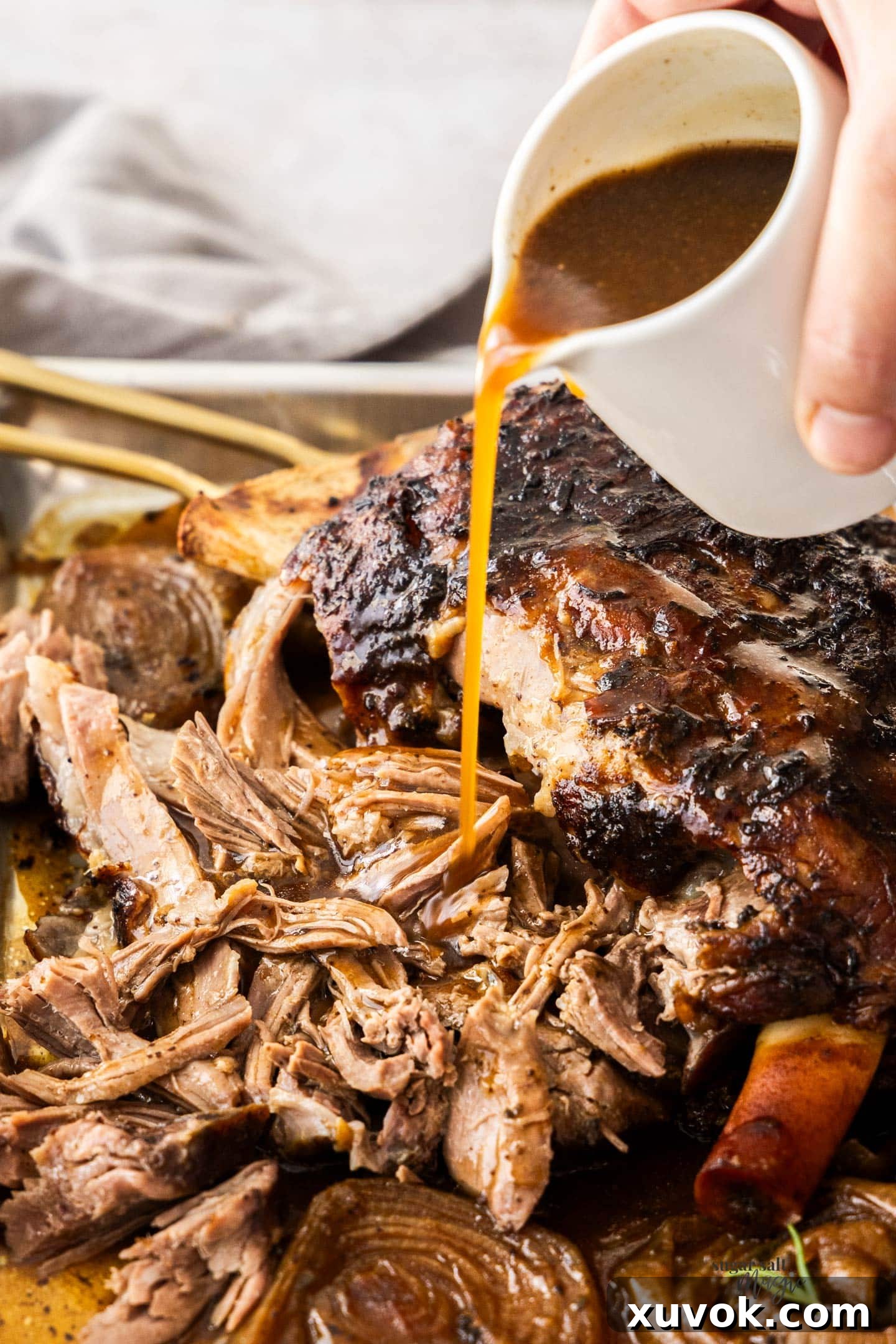 Rich gravy being poured from a small jug onto a serving of tender slow cooked pulled lamb.