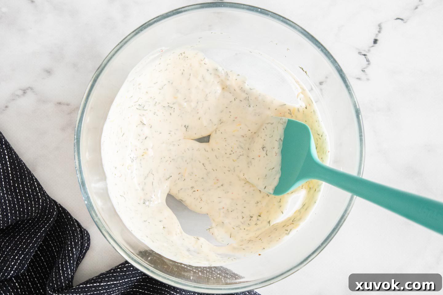 A perfectly blended creamy dressing for prawn rolls sits in a clear glass mixing bowl on a clean counter.