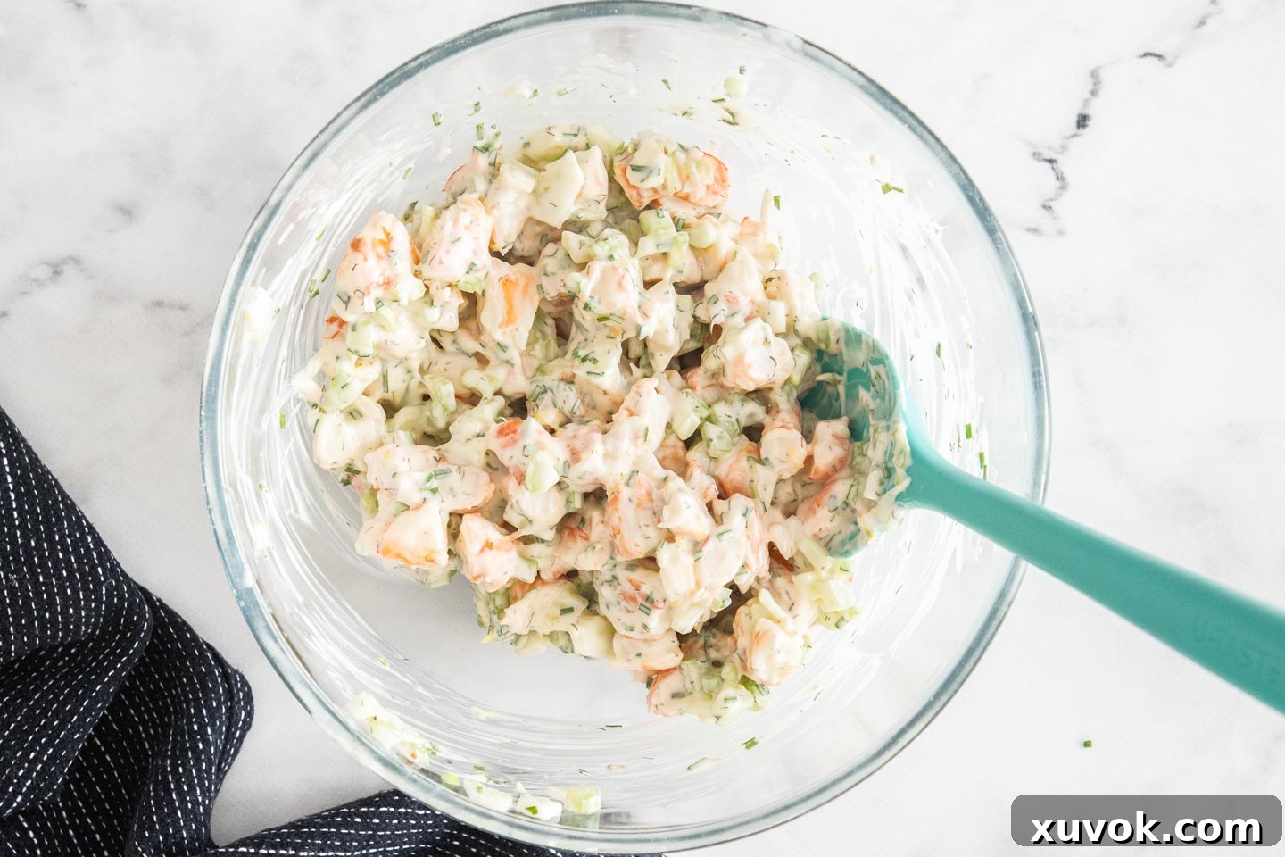 The creamy prawn roll filling, a vibrant mix of chopped prawns, celery, and herbs, expertly combined in a glass mixing bowl.