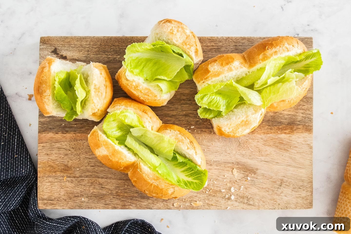 Four golden-brown bread rolls, split down the top and lined with fresh, crisp lettuce leaves, waiting for their delicious prawn filling.