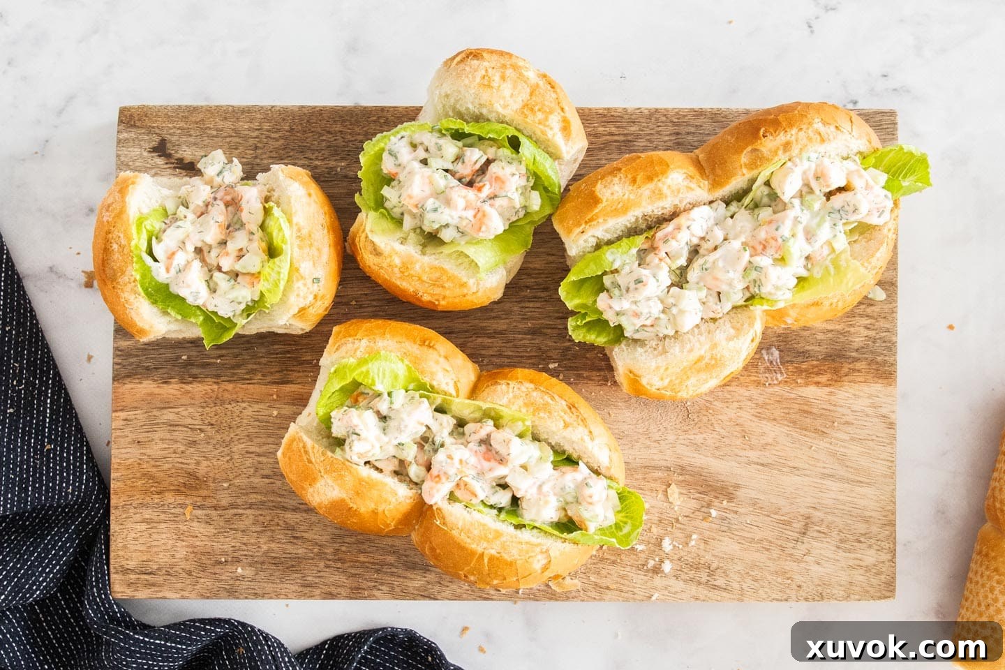 Four perfectly assembled prawn rolls, filled with creamy seafood and fresh lettuce, elegantly displayed on a wooden board, ready for enjoyment.