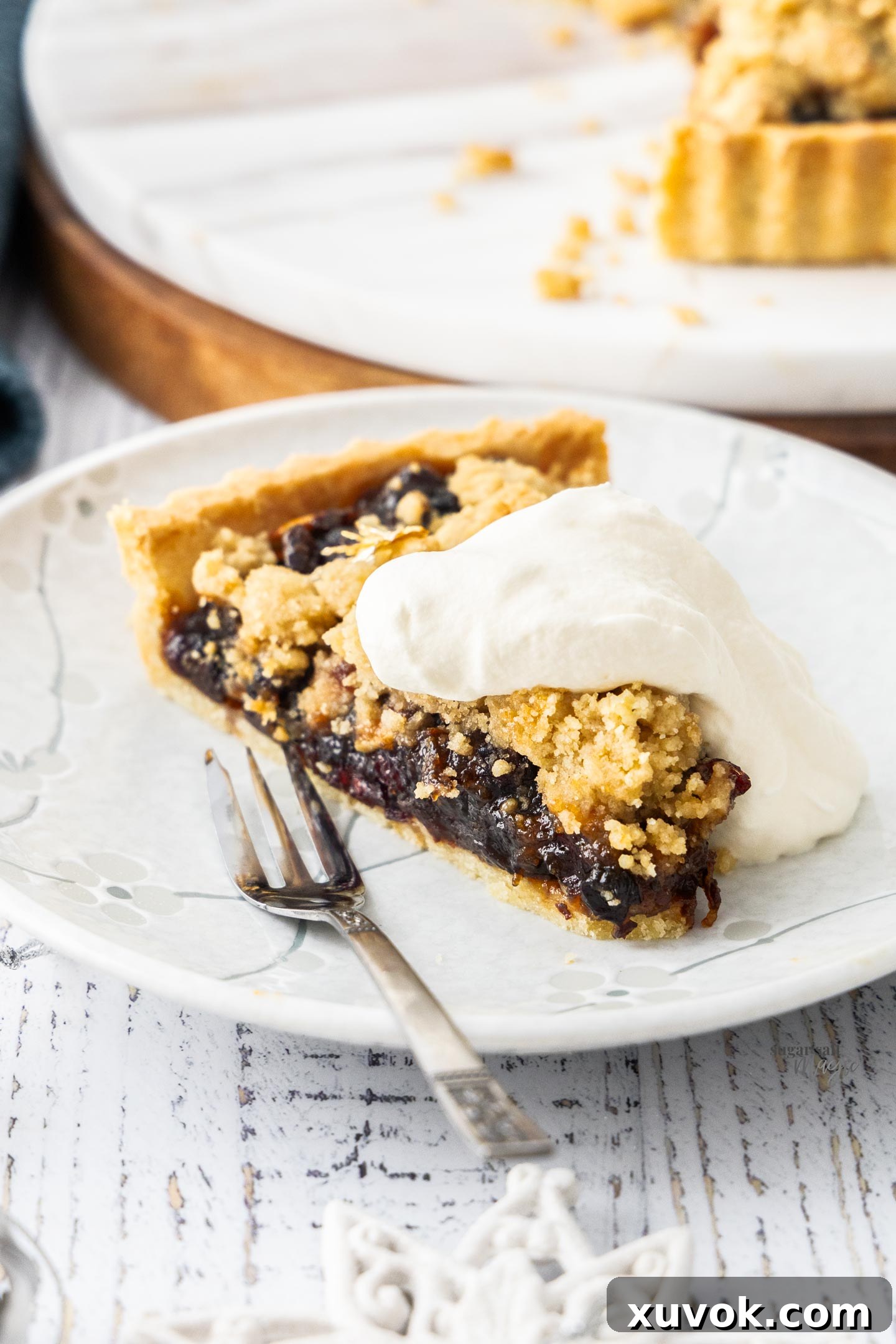 A slice of mince pie tart on a plate with a dollop of whipped cream.