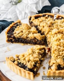 A fruit mince pie tart cut into slices on a marble platter.