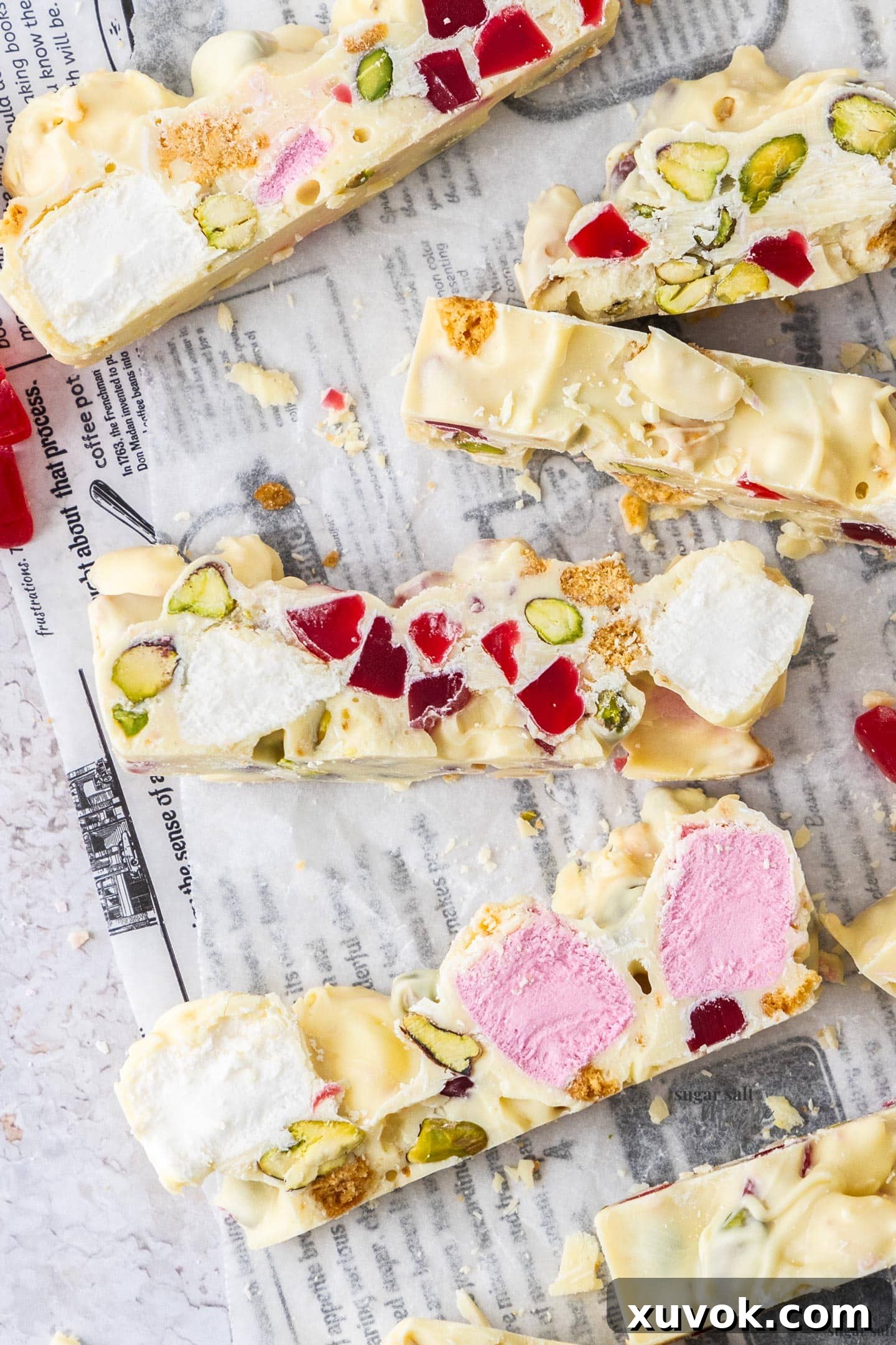 Slices of white chocolate rocky road on a sheet of baking paper showcasing the colorful ingredients within.