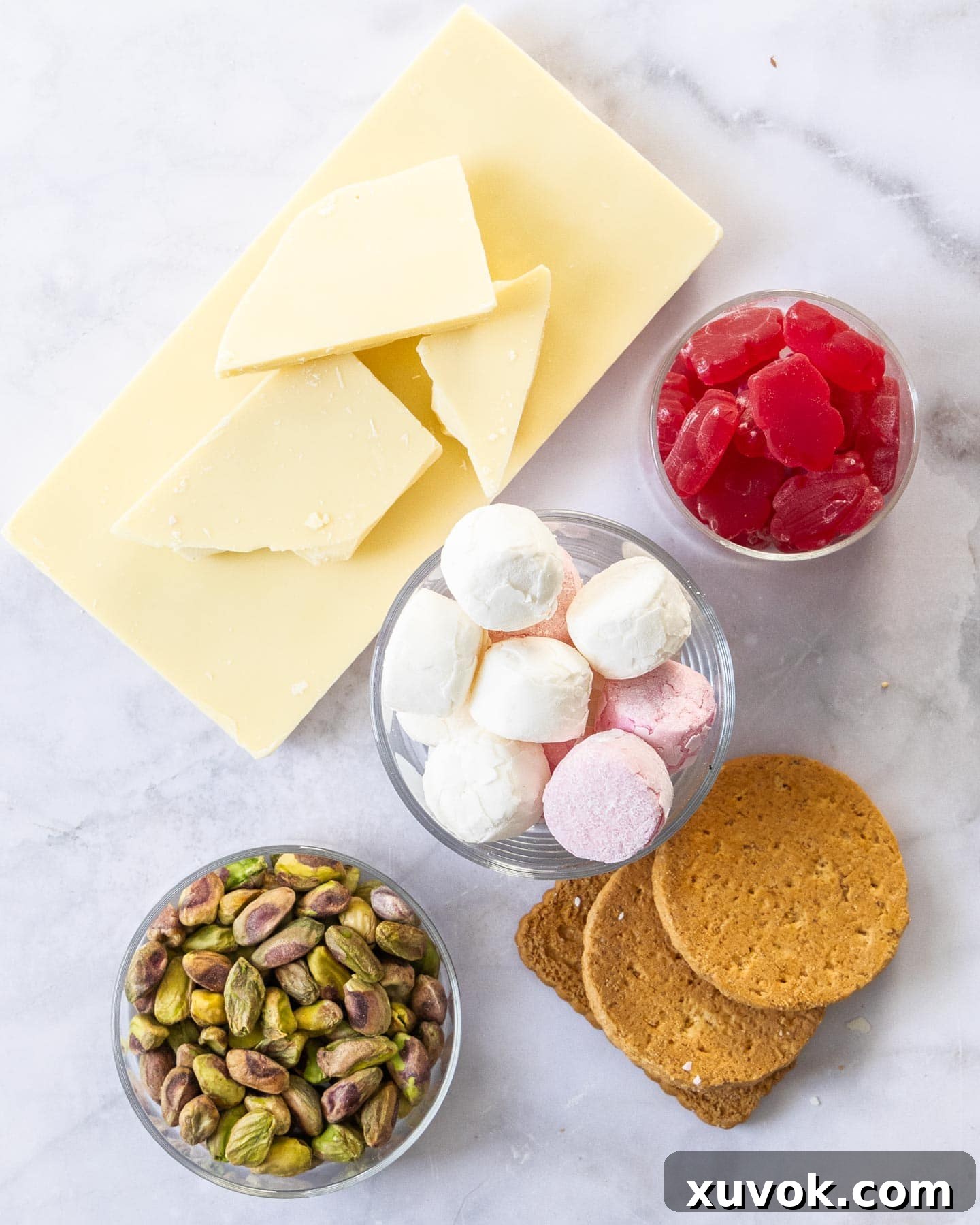 Ingredients laid out for making white chocolate rocky road, including white chocolate, marshmallows, candies, nuts, and cookies.