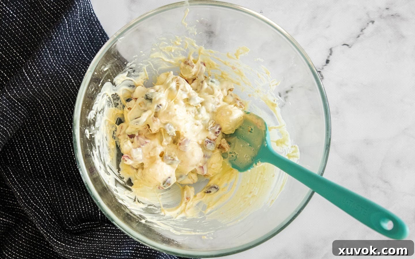 Melted white chocolate mixed with marshmallows, candies, nuts, and cookies in a mixing bowl.