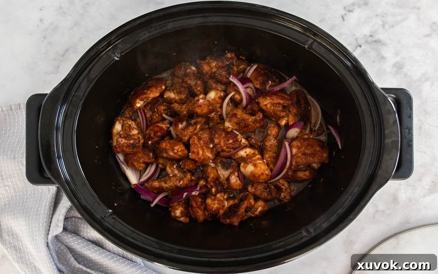 Chicken, onion, garlic, and stock simmering in a slow cooker bowl.