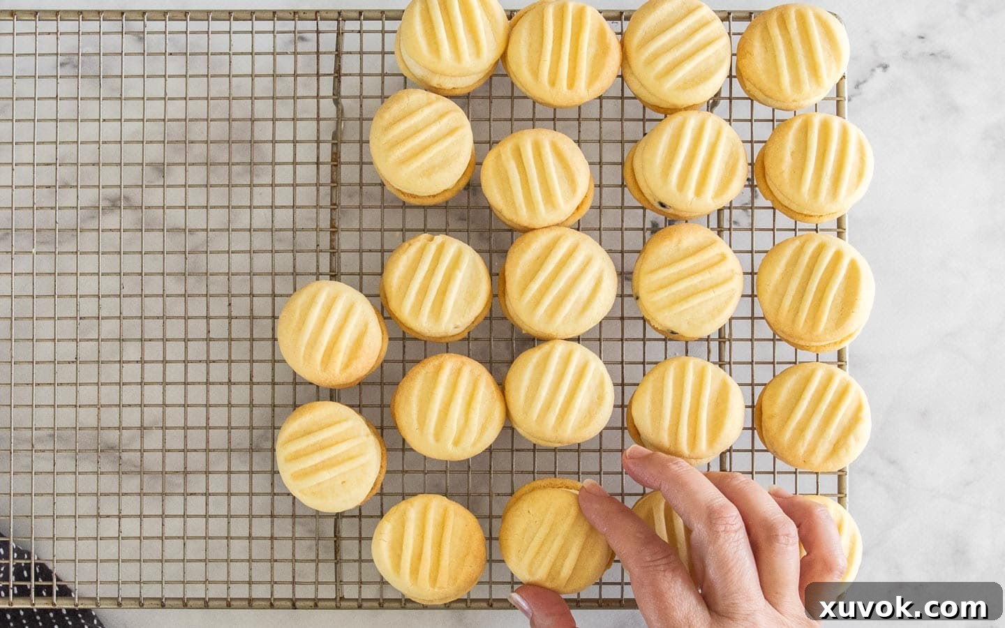 The cookies being topped with a second one to sandwich the buttercream inside, completing the melting moment.