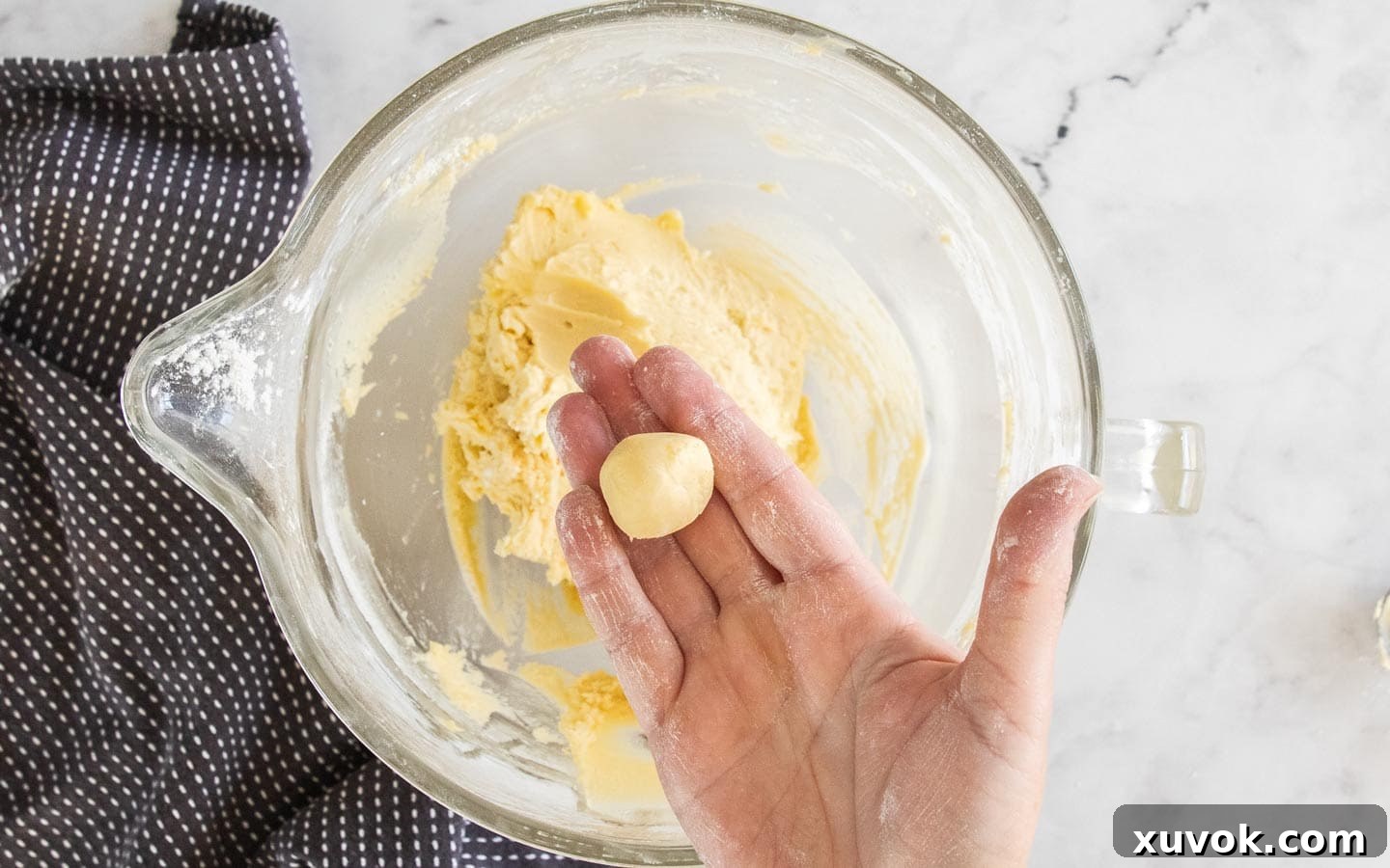 A hand gently holding a perfectly rolled ball of cookie dough.