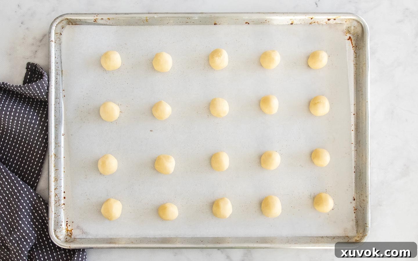 Rows of cookie dough balls meticulously placed on a baking sheet, ready for the fork imprint.