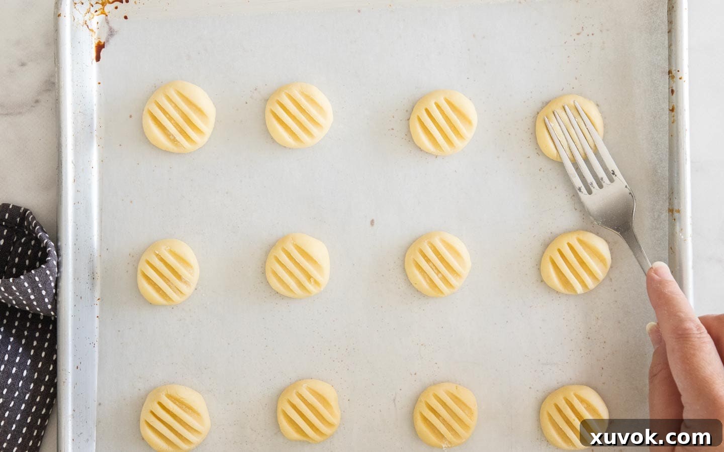 A fork being pressed down onto a cookie dough ball, creating the iconic ridged design.