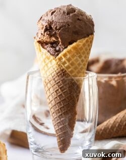 A waffle cone filled with scoops of chocolate ice cream standing up in a glass.