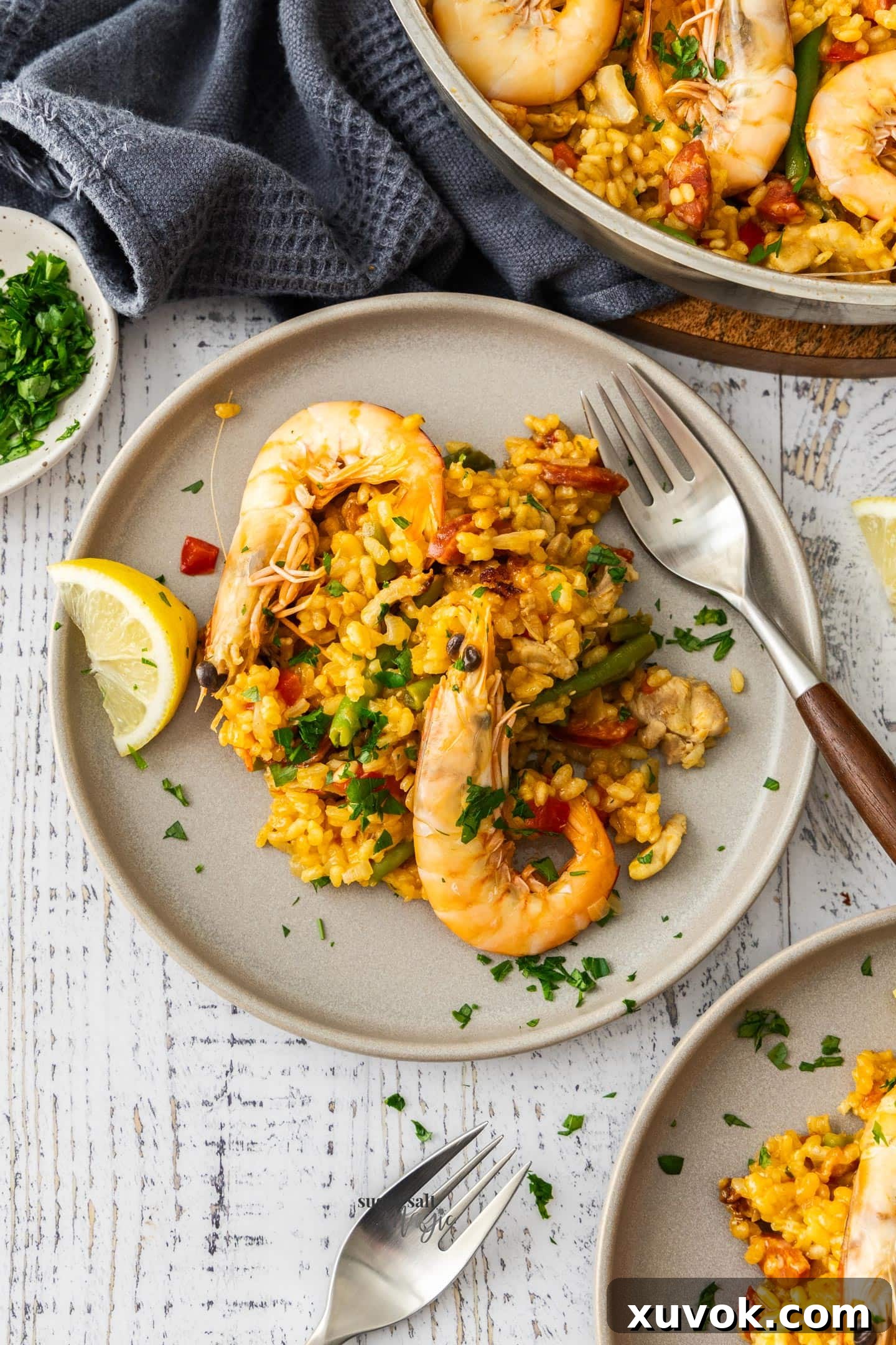 A serving of chicken and chorizo paella with 2 prawns on a dinner plate.