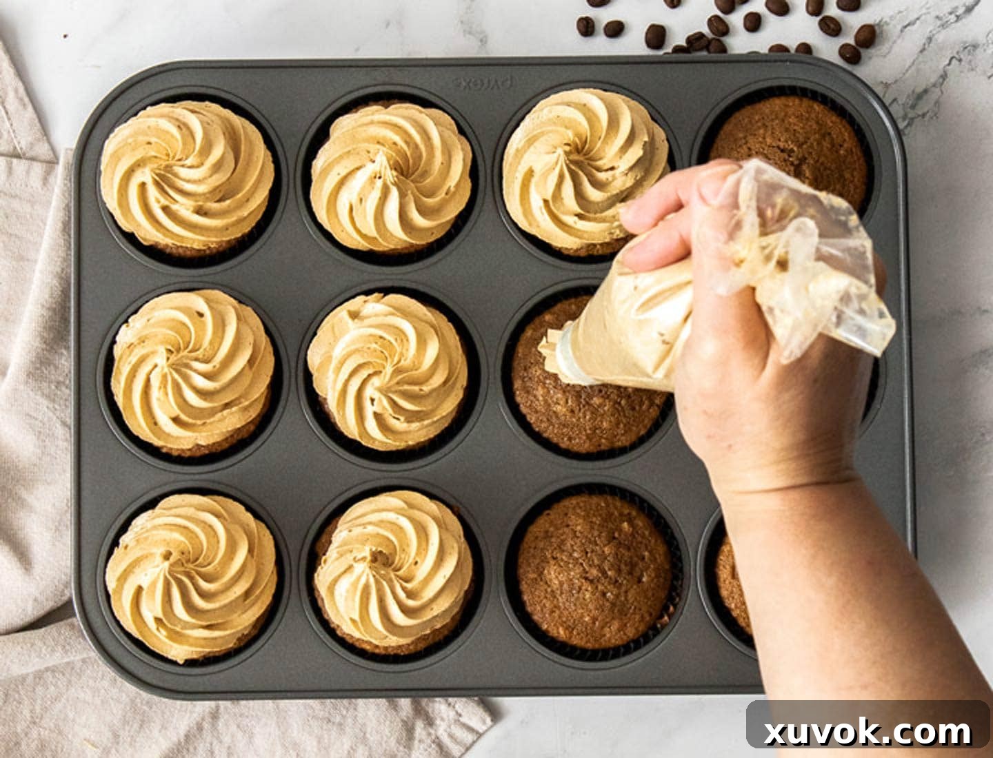 Coffee buttercream being piped onto coffee cupcakes.