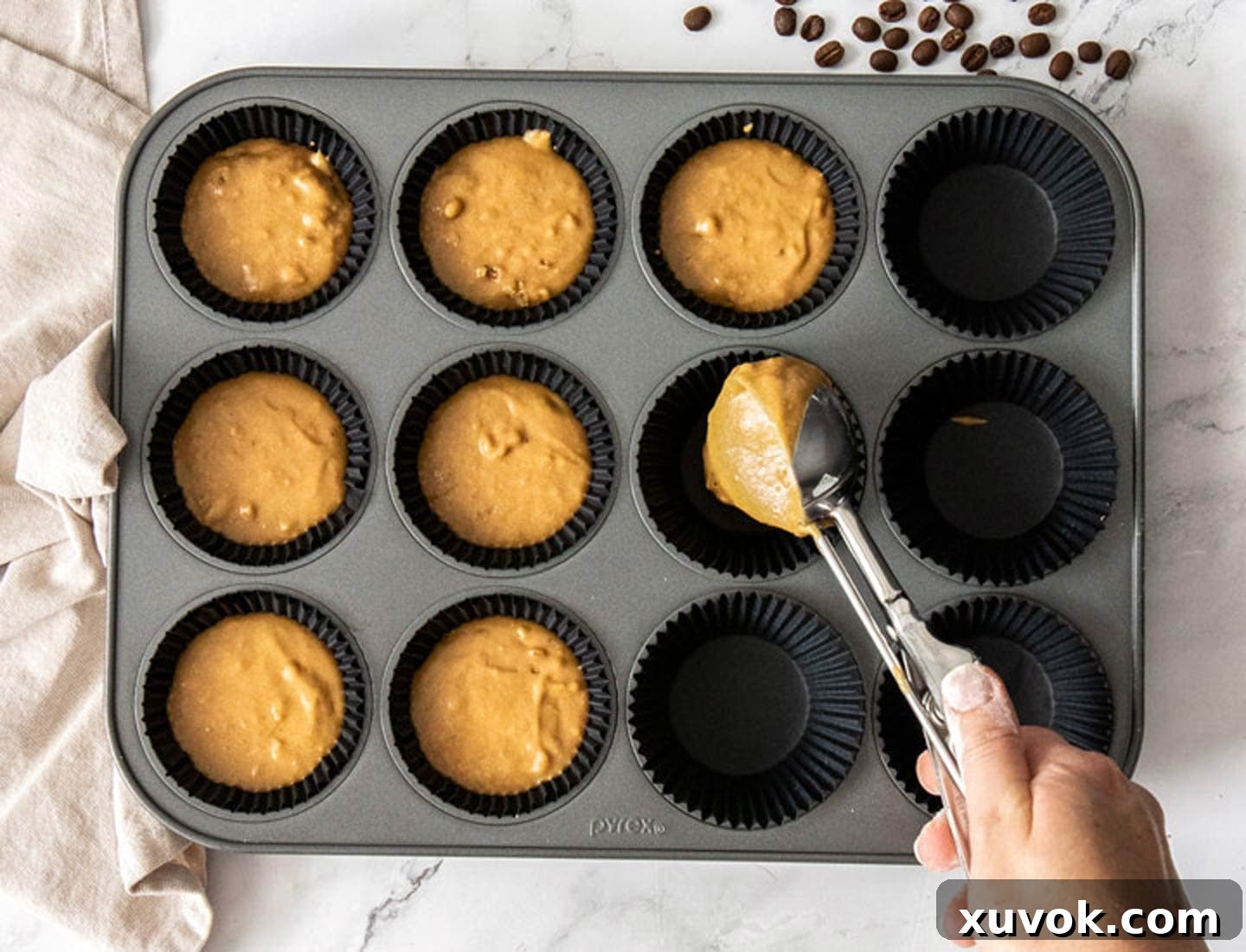 The cupcake batter being scooped into cupcake liners in a metal muffin pan.