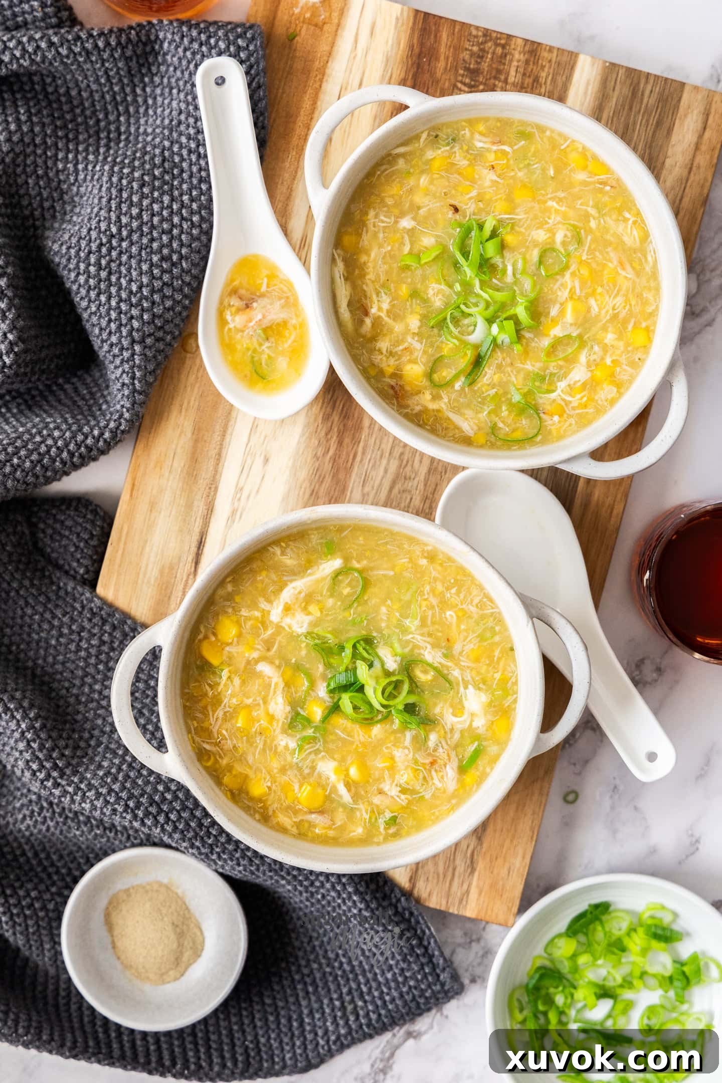 Top down view of two bowls of corn and crab soup on a wooden board.