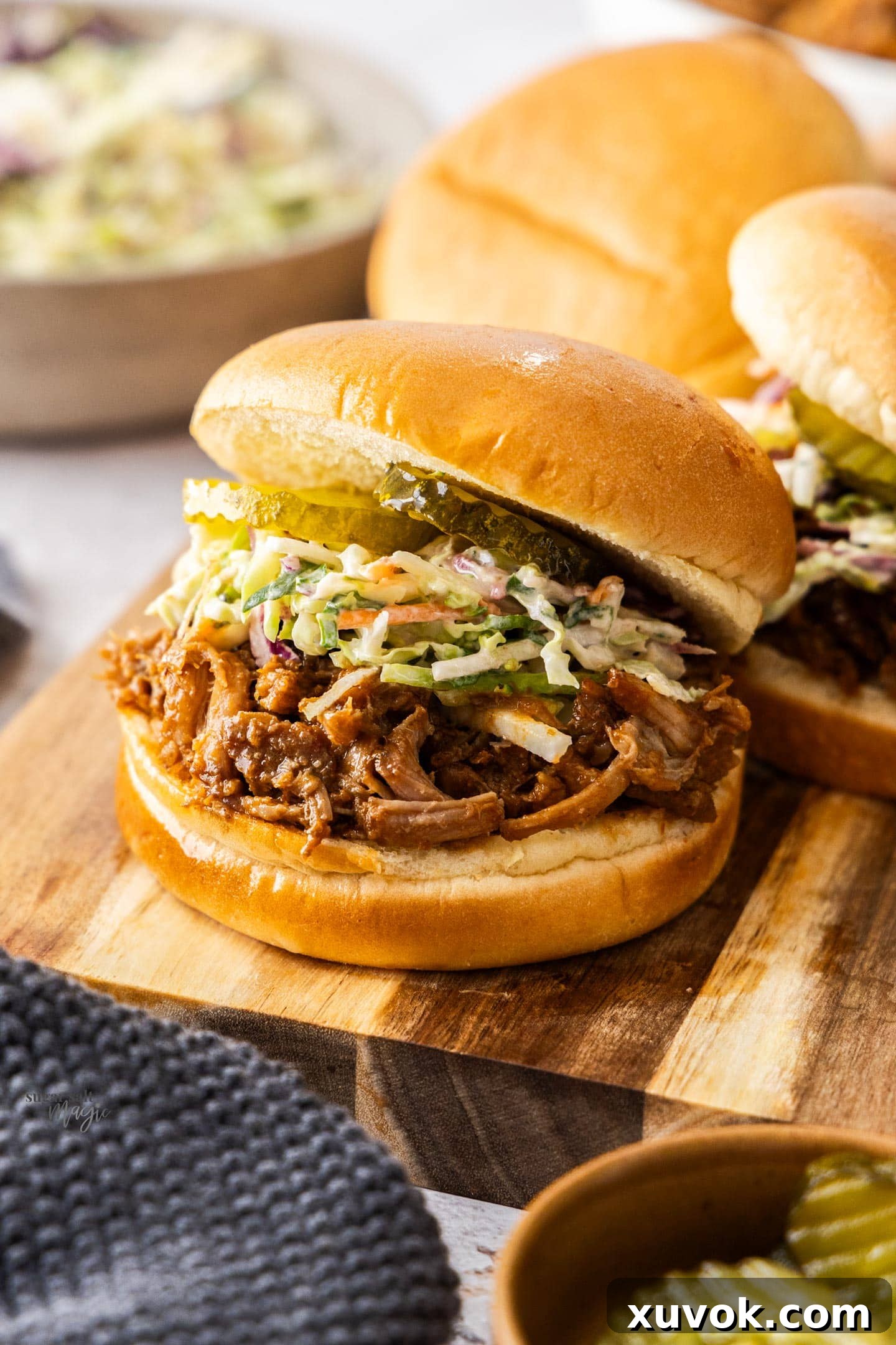 A burger bun filled with pulled pork, coleslaw and gherkins on a wooden platter.