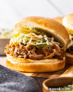 A burger bun filled with pulled pork, coleslaw and gherkins on a wooden platter.