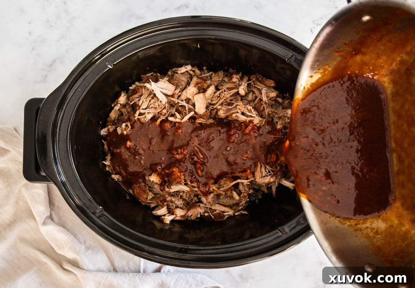 The sauce being poured over the shredded pork.