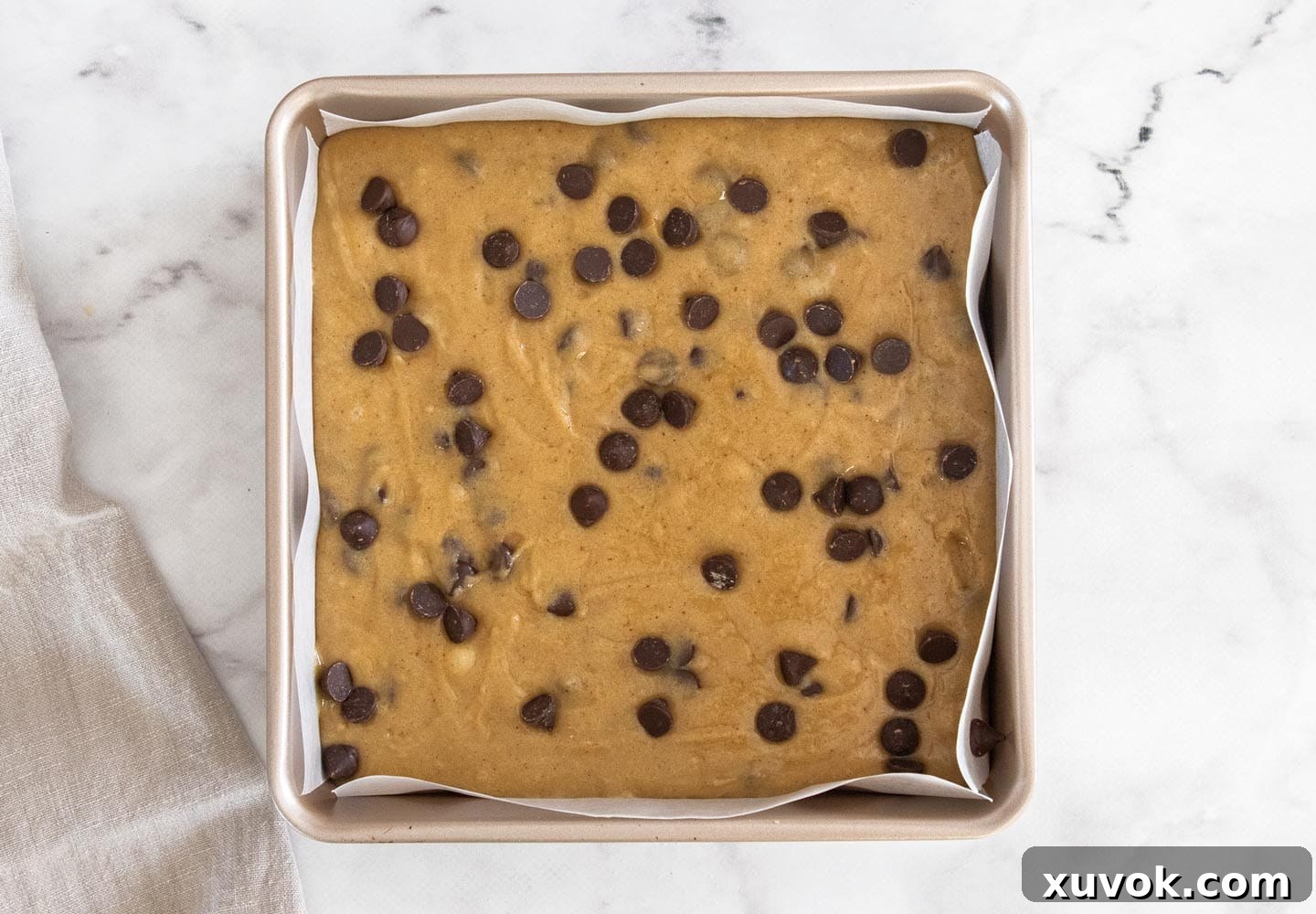 Blondie batter smoothed into an 8-inch square baking pan, topped with extra chocolate chips.