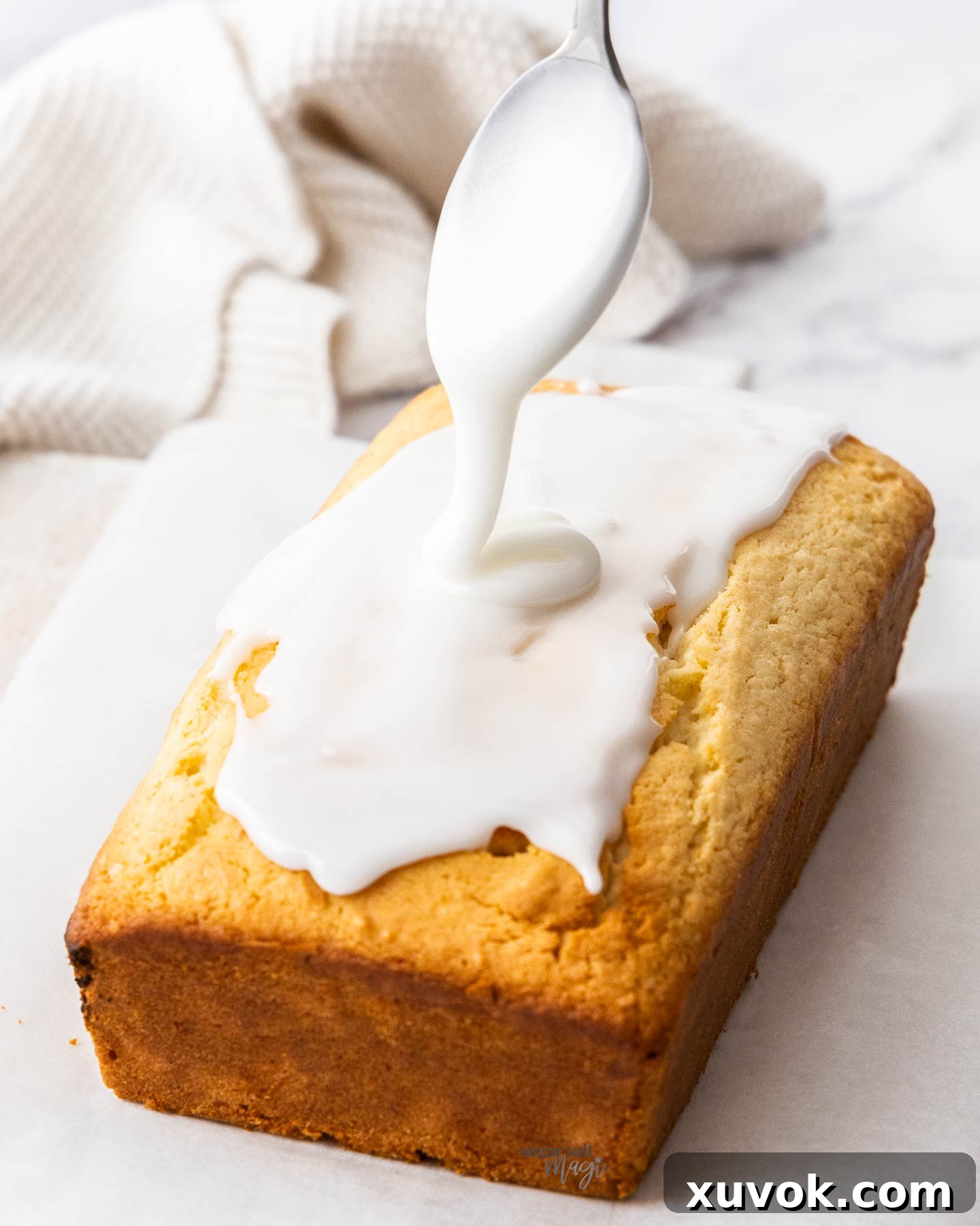 Thick lemon icing being artfully drizzled over a cooled lemon loaf cake, gracefully coating the top and cascading down the sides.