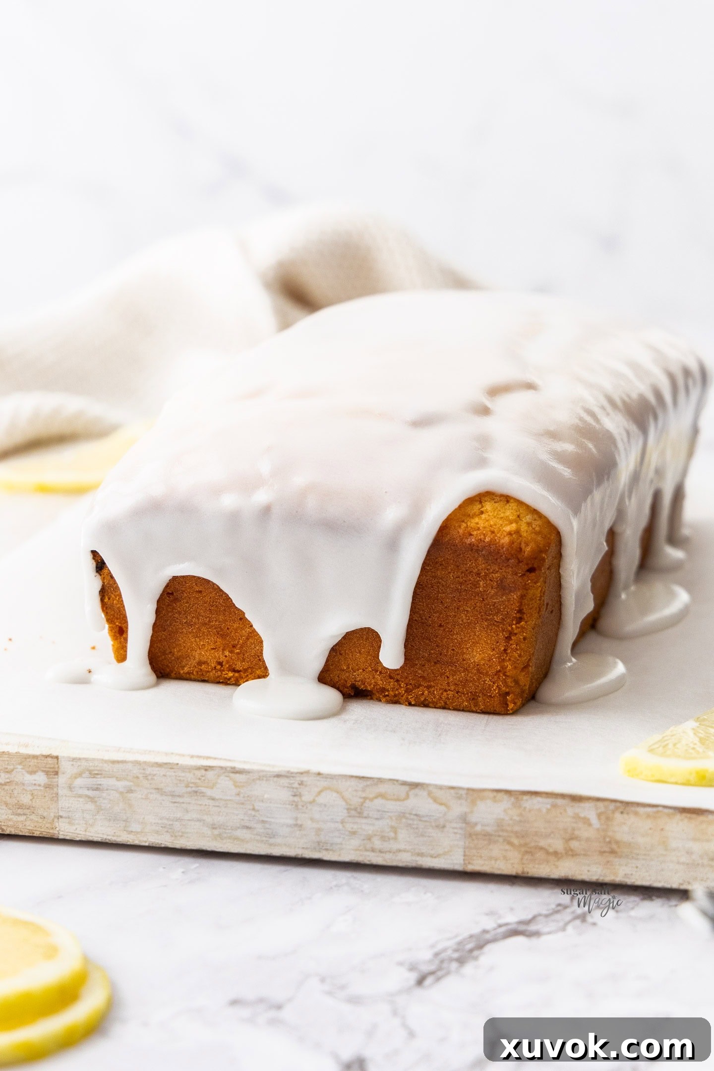 A perfectly baked and glazed lemon loaf cake, still whole, resting on a wire cooling rack, ready to be sliced and served.