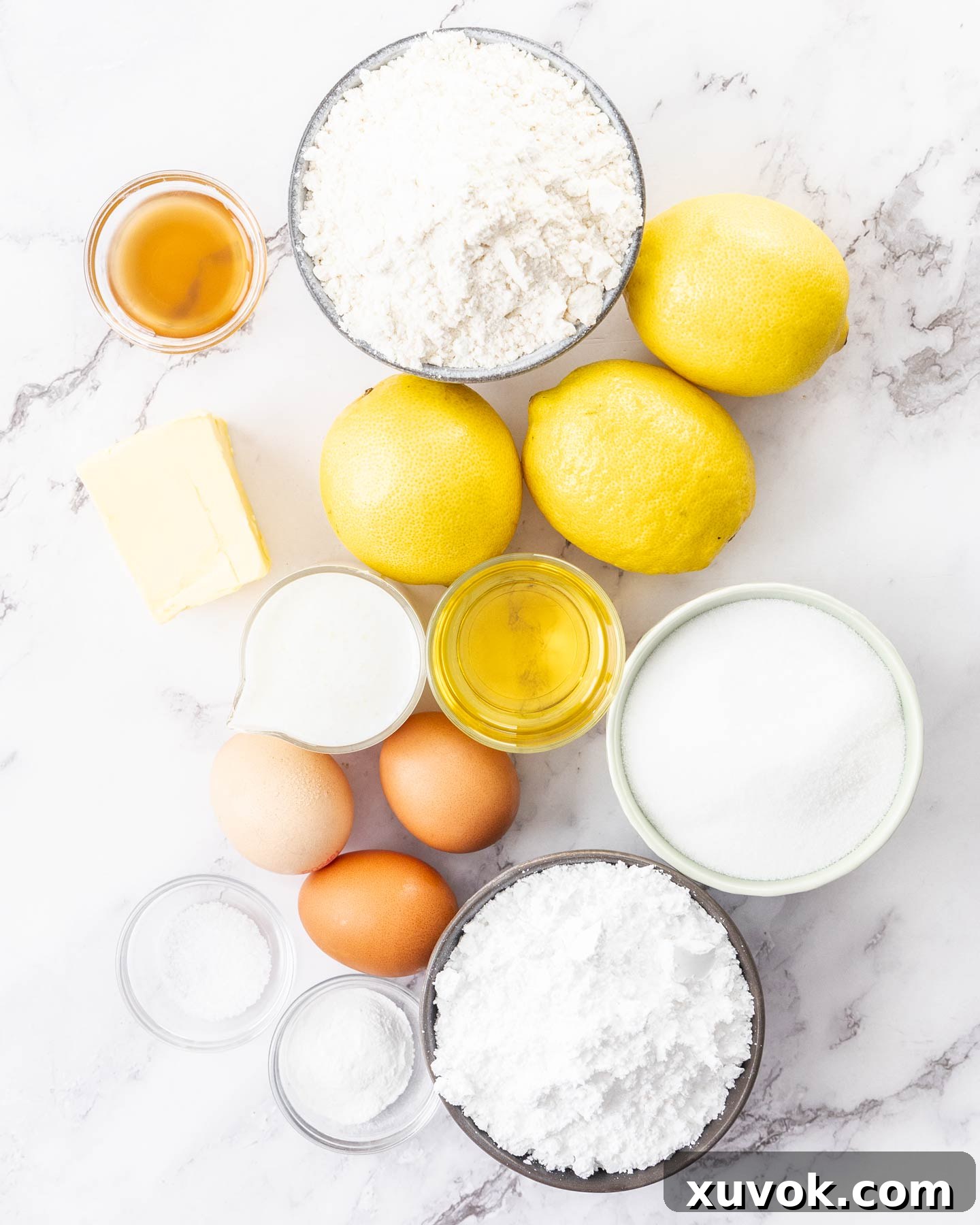 A beautifully arranged spread of fresh ingredients for lemon loaf cake on a sophisticated marble surface, highlighting the vibrant lemons, butter, eggs, and flour.