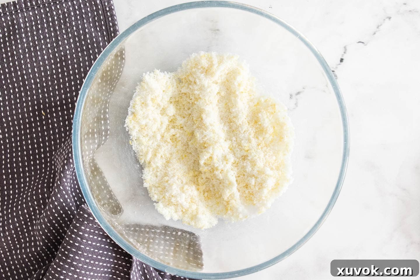 Close-up of lemon zest being rubbed into white granulated sugar in a mixing bowl, creating fragrant lemon sugar.