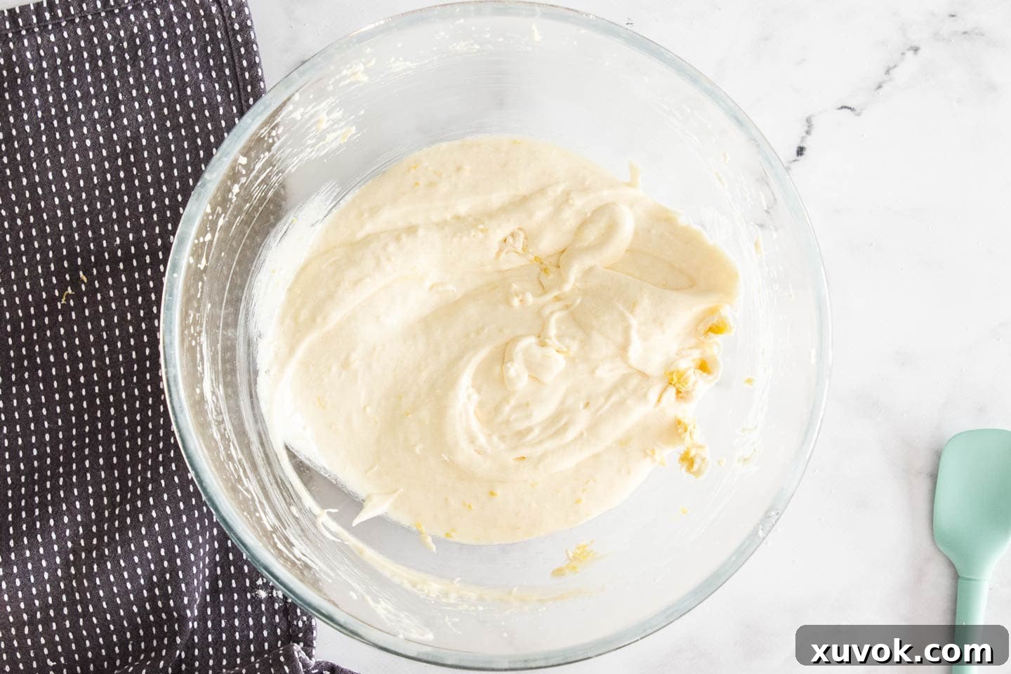 Eggs beaten into the creamy lemon sugar and butter mixture in a mixing bowl, creating a smooth, pale batter.