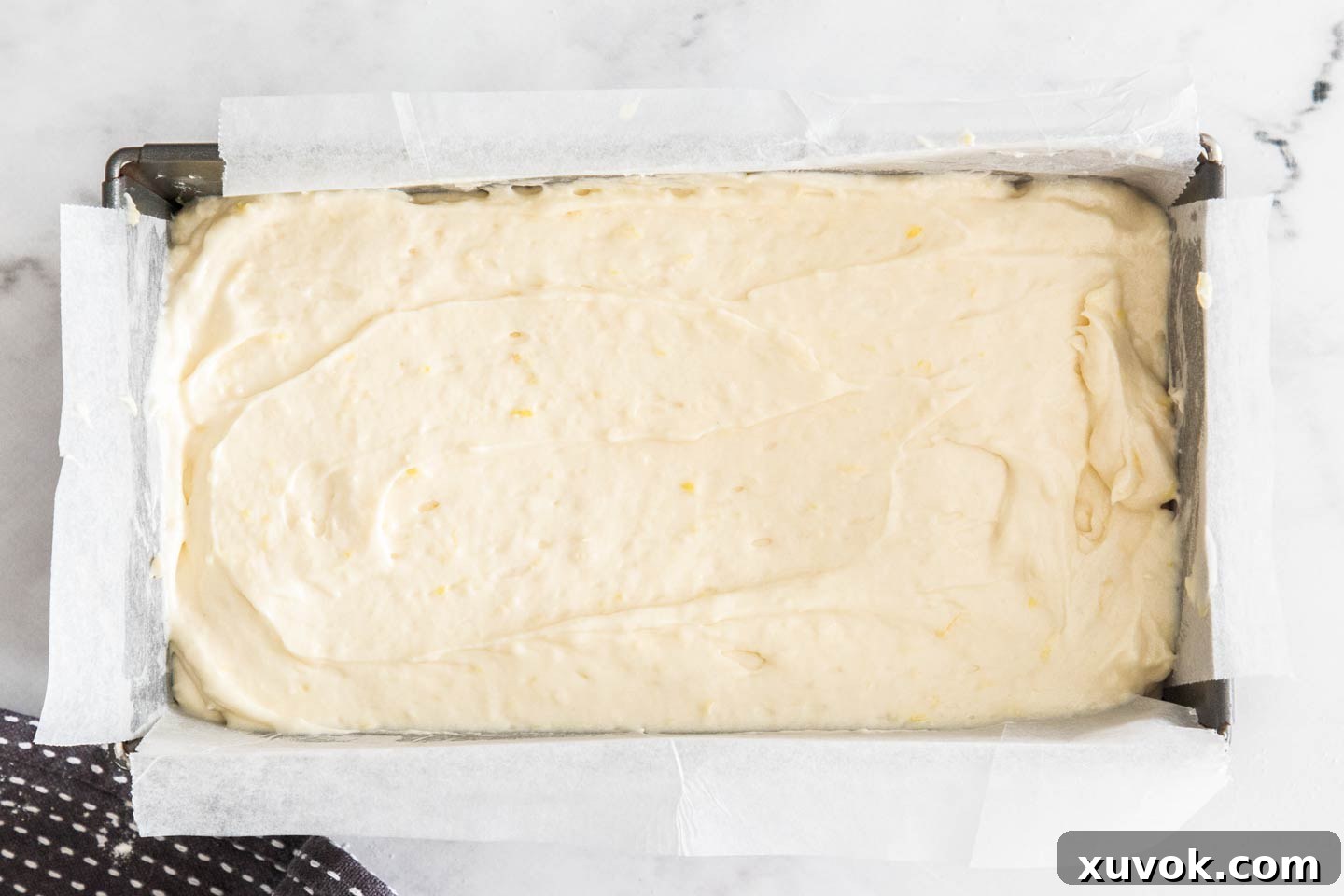 Freshly poured lemon loaf cake batter settled evenly in a lined loaf pan, ready to be baked to golden perfection.