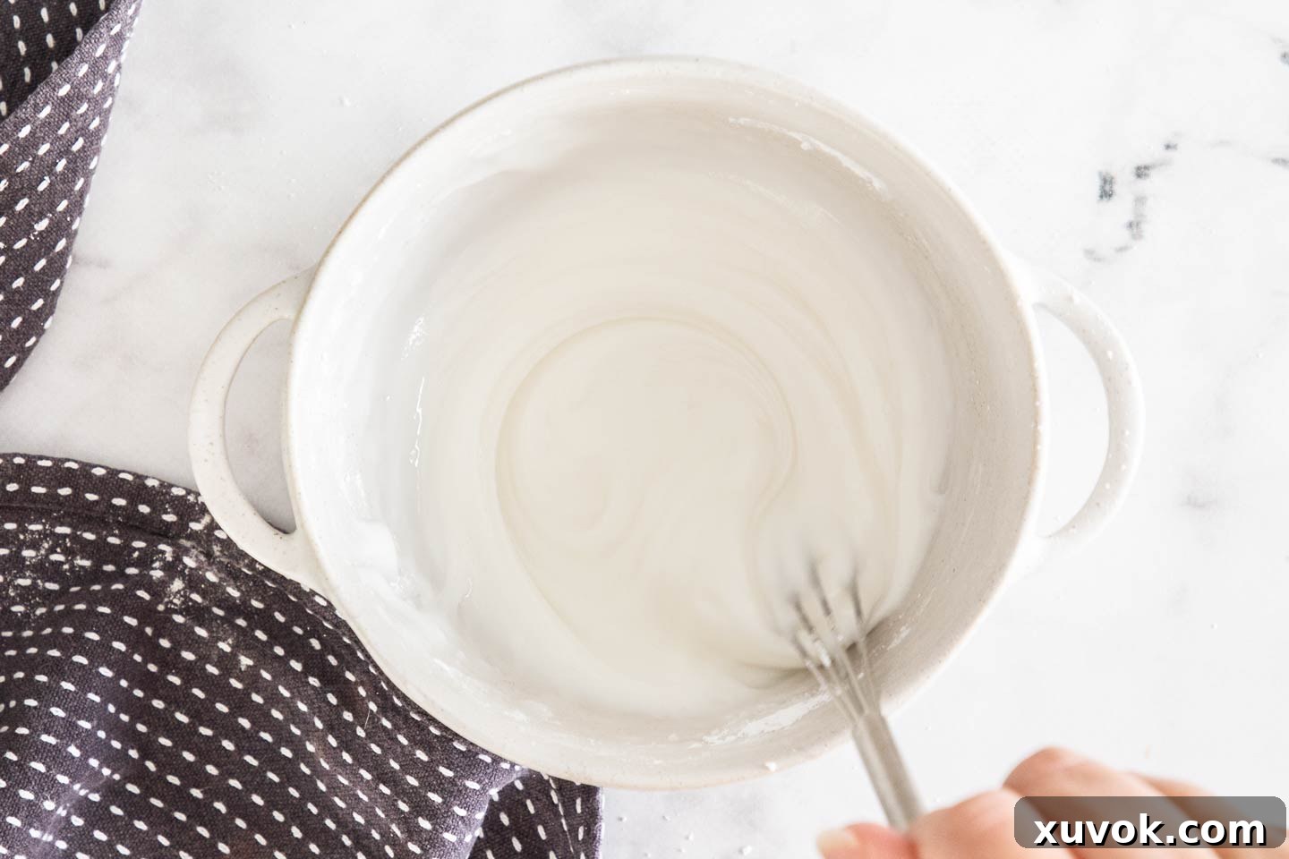 Lemon icing being whisked vigorously in a white ceramic bowl, showing its smooth and creamy texture.