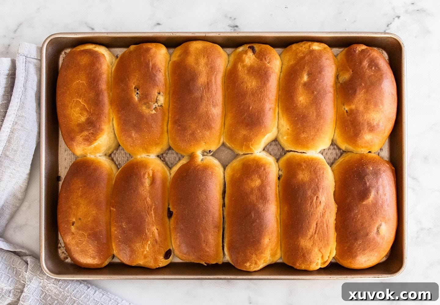 Top down view of 12 golden-brown baked finger buns cooling on a baking tray, perfectly risen and ready for icing.