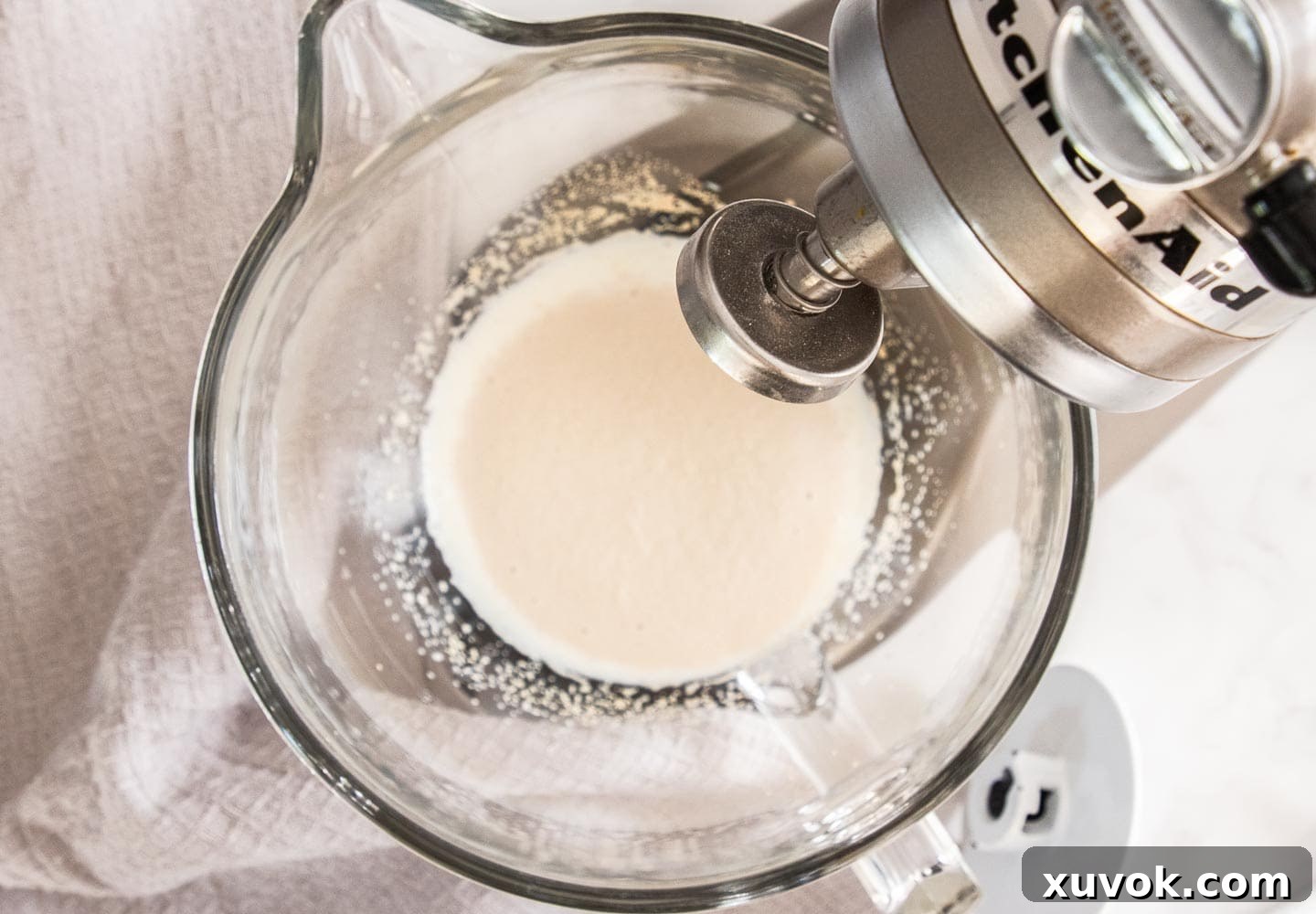 Close-up of yeast blooming in a bowl with warm milk and sugar, showing a frothy, active surface.