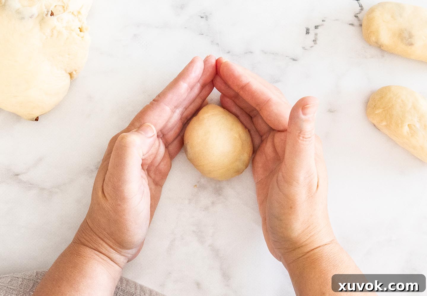 A hand expertly smoothing a small ball of finger bun dough against a work surface, demonstrating the shaping technique.