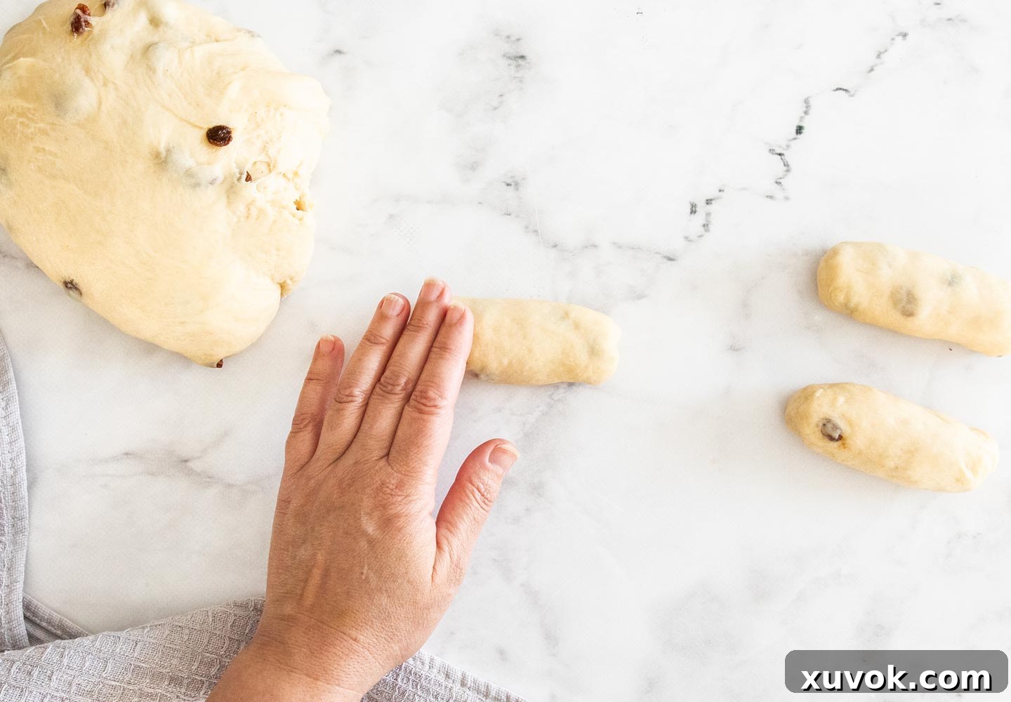 A hand skillfully rolling a piece of finger bun dough into an elongated log shape, preparing it for its final prove.
