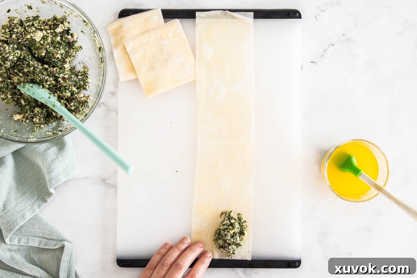 The spinach and feta filling carefully placed on the bottom corner of a long filo strip, ready for folding.