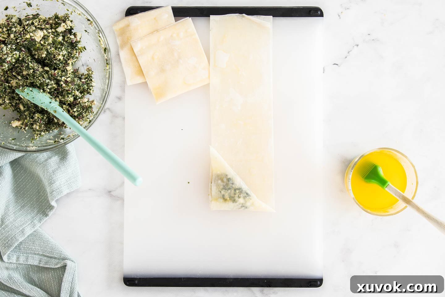 The filo triangle being folded upwards, continuing the intricate layering process to secure the filling.