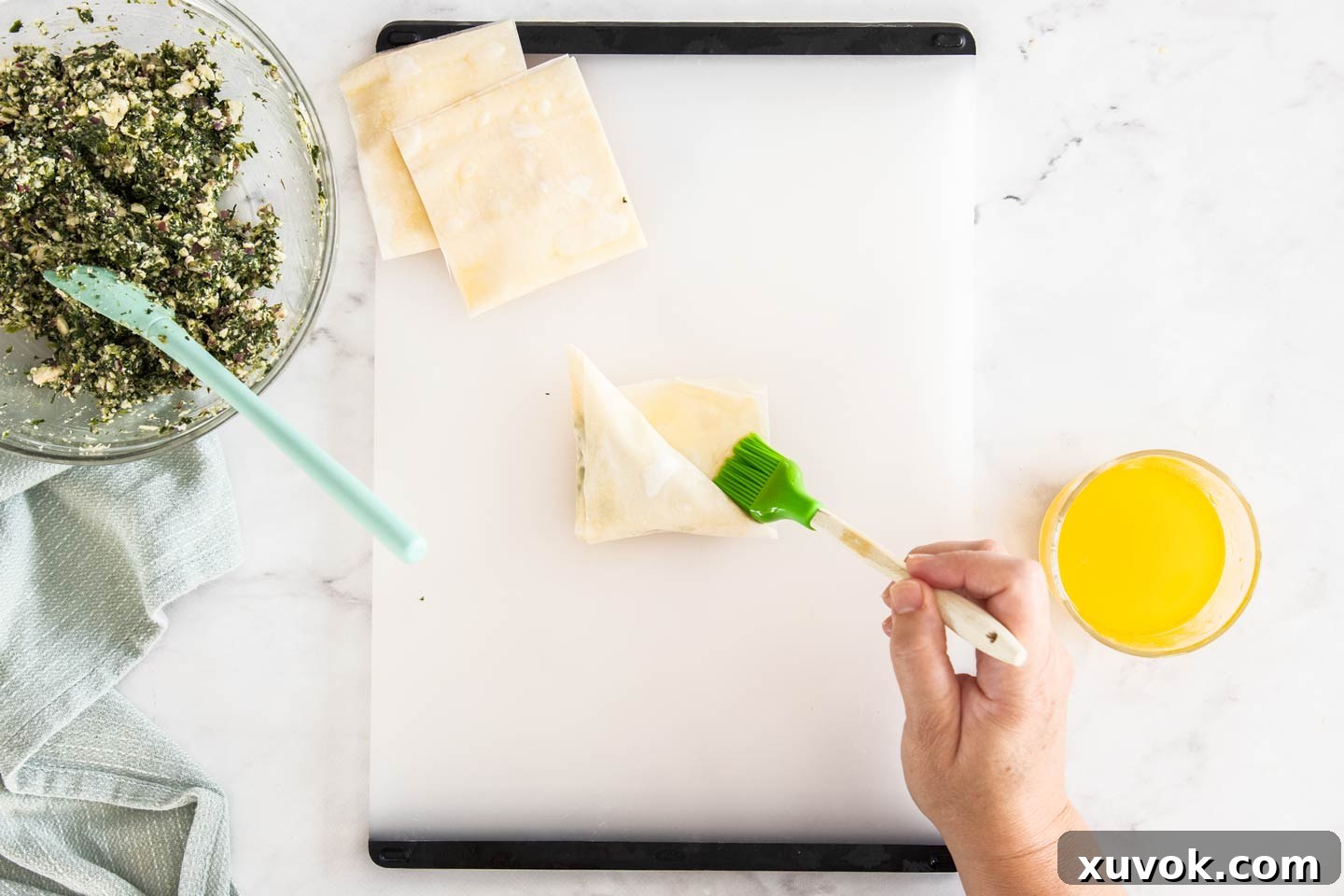 A brush applying melted butter to the final edge of the filo pastry, sealing the triangle before baking.