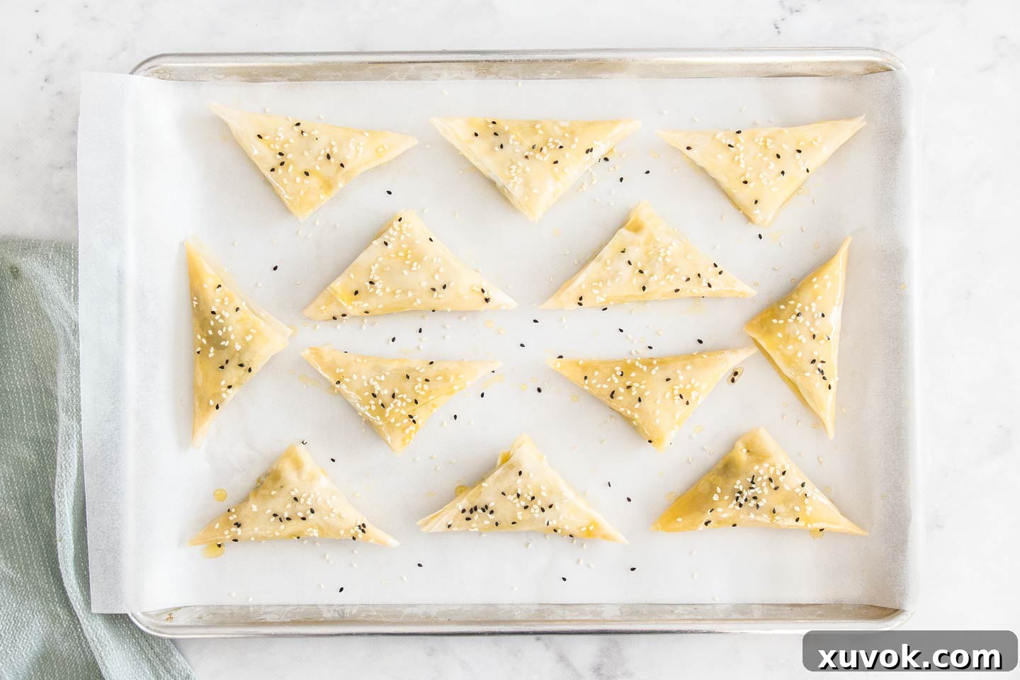 Spinach and feta parcels arranged neatly on a baking tray, brushed with butter and sprinkled with sesame seeds, ready for the oven.