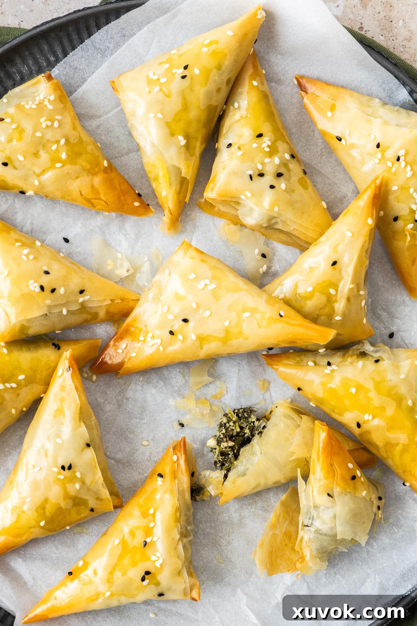 A top-down view of a fresh batch of golden-brown spanakopita triangles arranged on a metal tray, ready to be served.