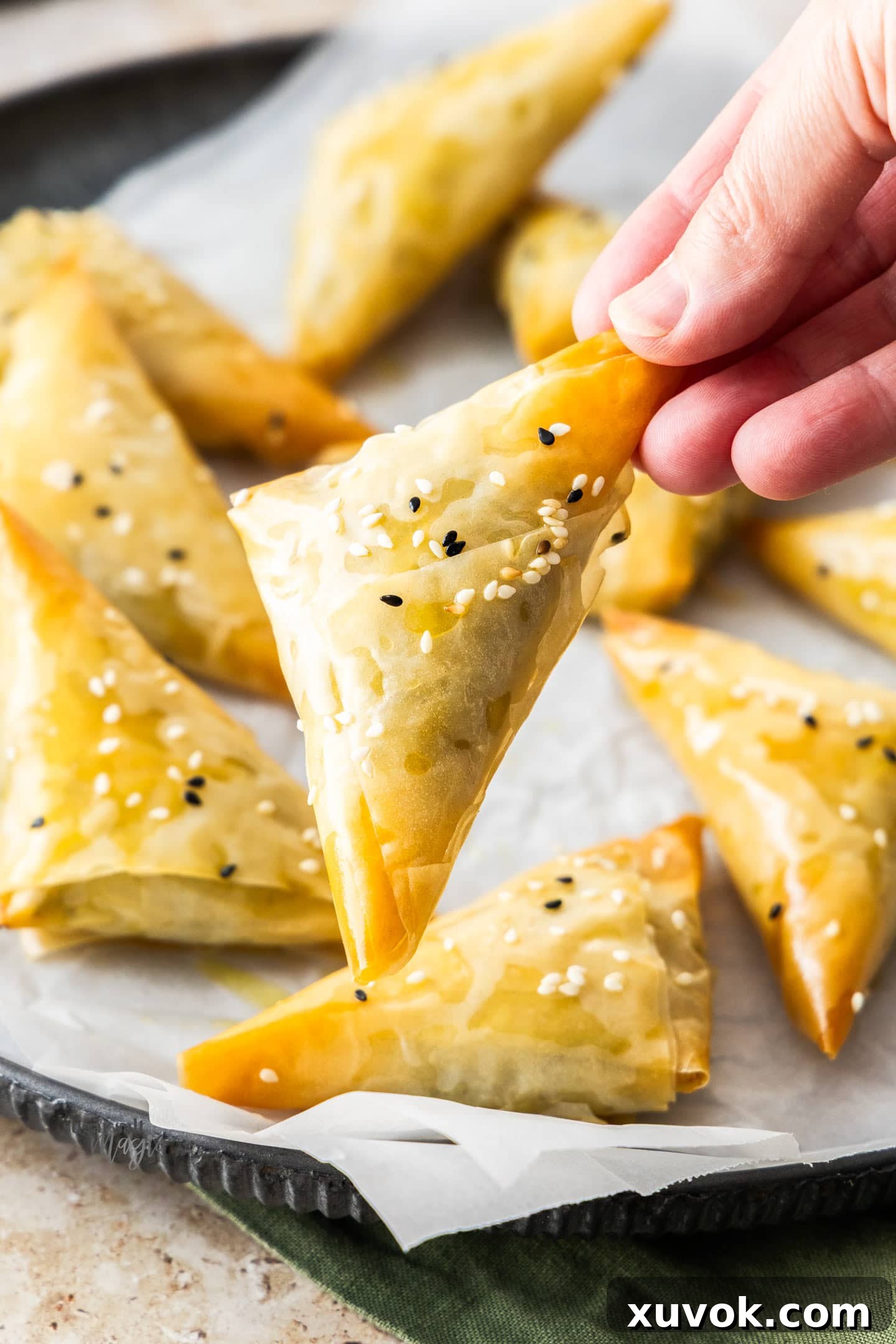 A hand gently holding a golden-brown spinach and feta parcel, showcasing its crisp, flaky exterior.