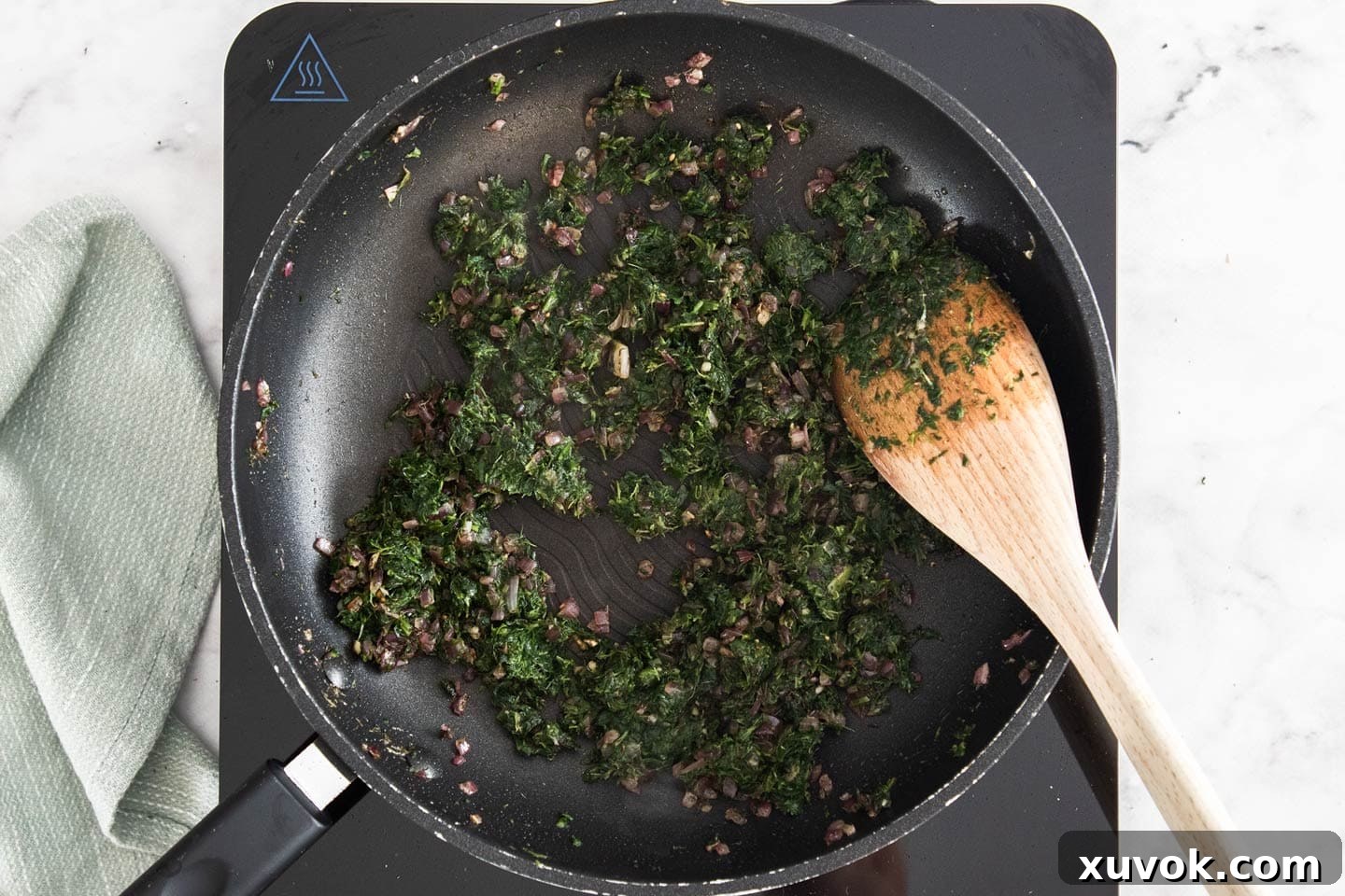 Sautéing spinach and onion in a frying pan over medium heat.