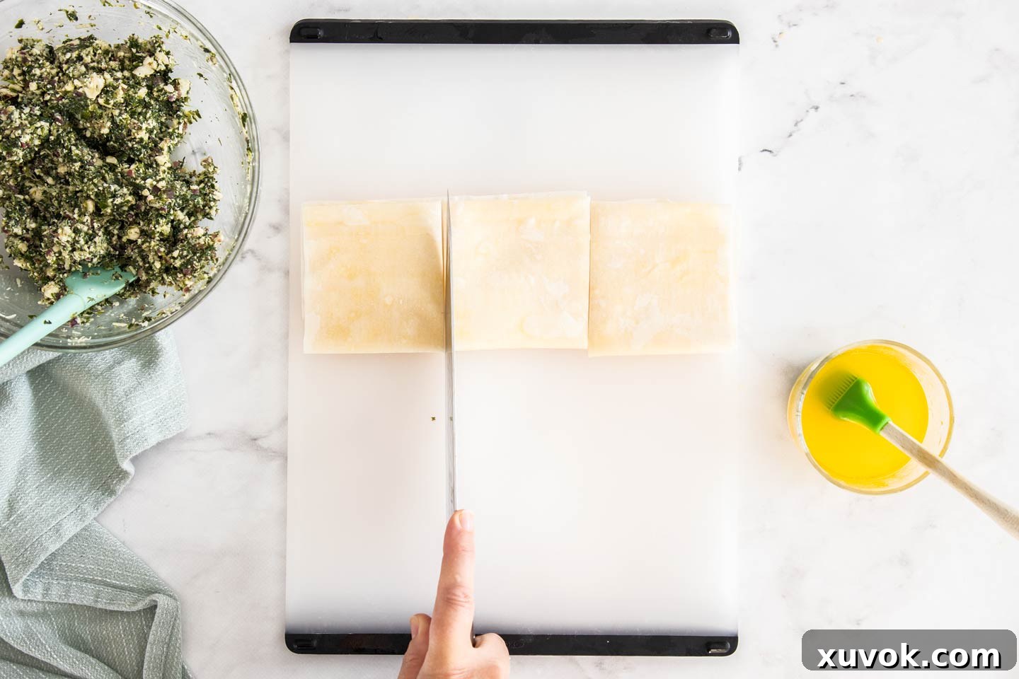 Filo pastry folded again and a knife poised to cut it into three equal pieces for individual parcels.