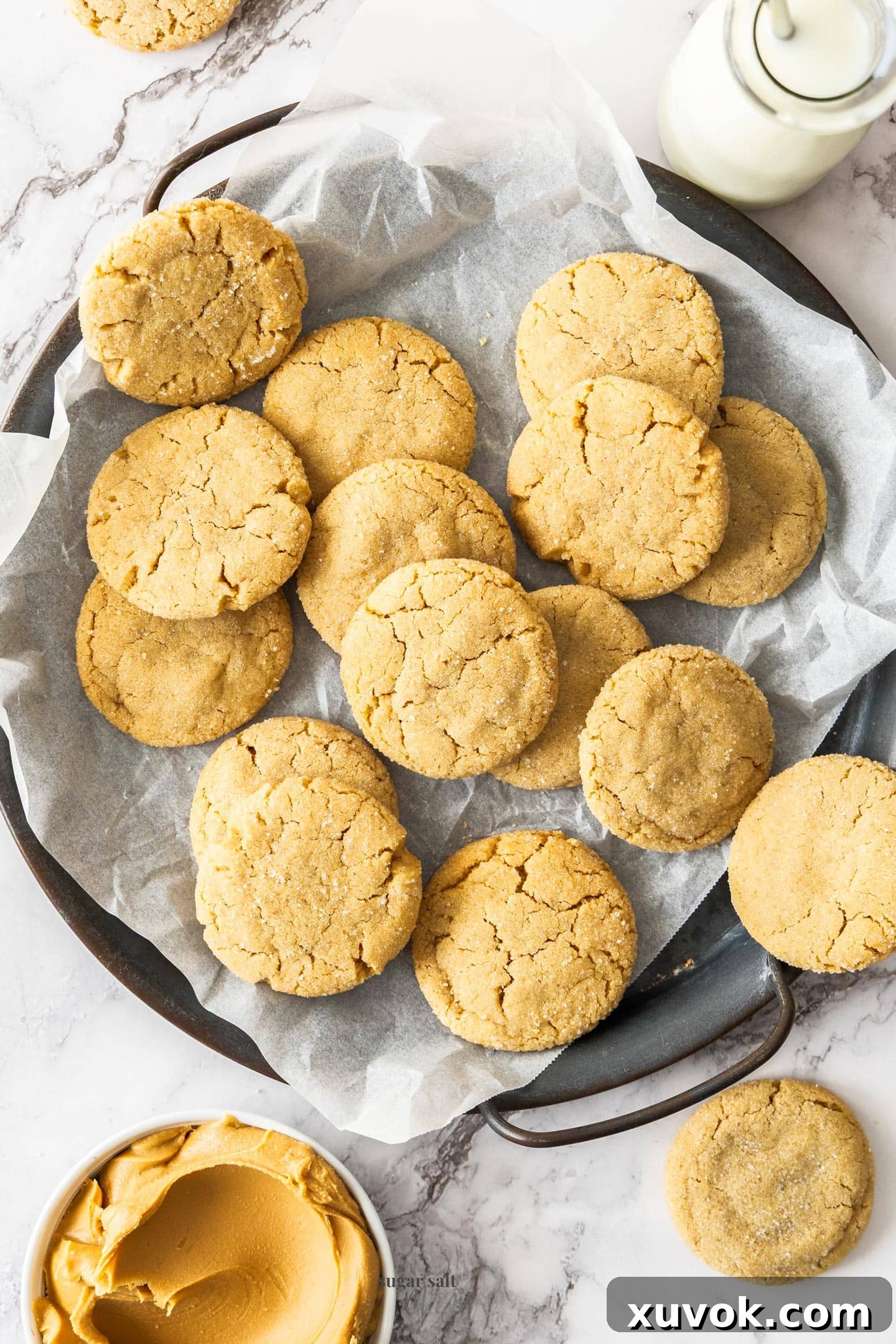A batch of browned butter peanut butter cookies on a metal tray with a glass of milk next to it, highlighting their crisp edges and soft centers.