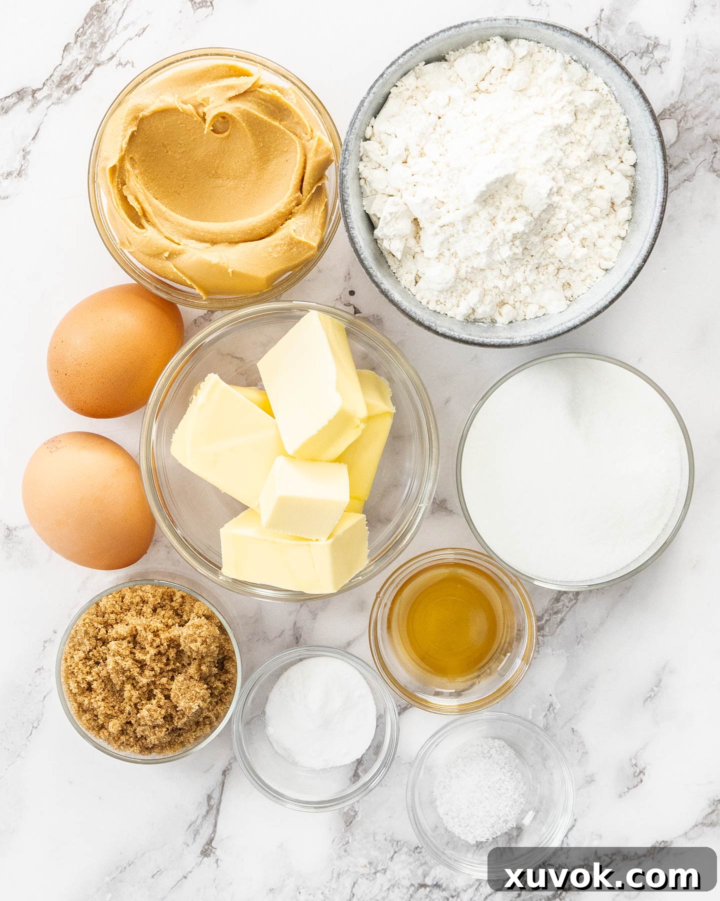 A beautifully arranged selection of ingredients for browned butter peanut butter cookies on a pristine marble surface, ready for baking.