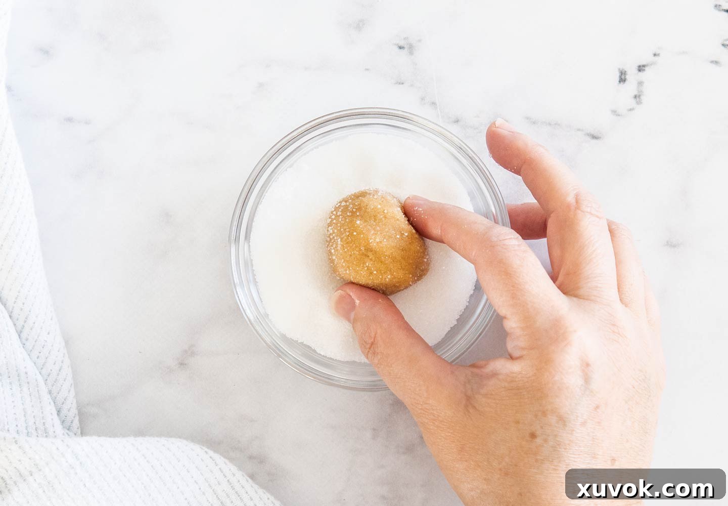 A hand gently rolling a ball of peanut butter cookie dough in granulated sugar, preparing it for baking.