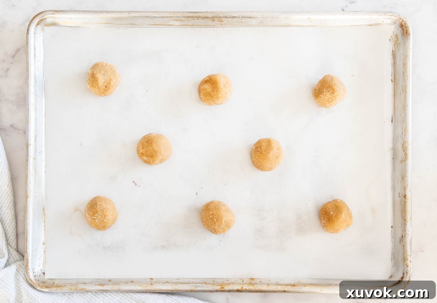 Perfectly portioned and sugared cookie dough balls artfully arranged on a baking sheet, patiently awaiting their transformation in the oven.