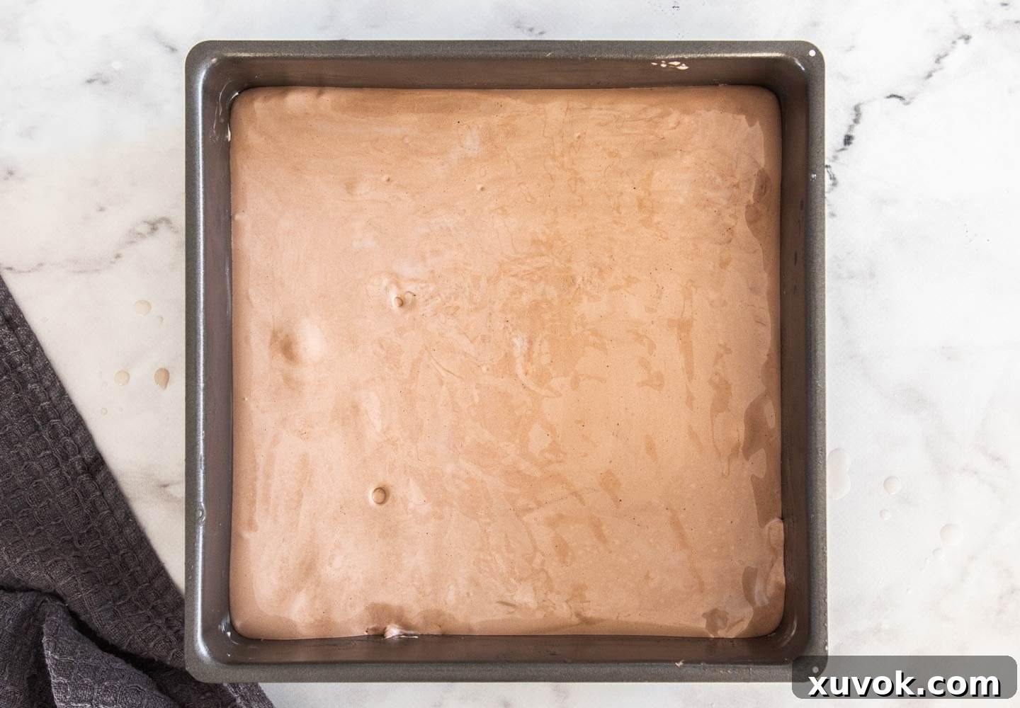 The chocolate marshmallow mixture spread evenly in a baking pan, ready for its cocoa sugar dusting.