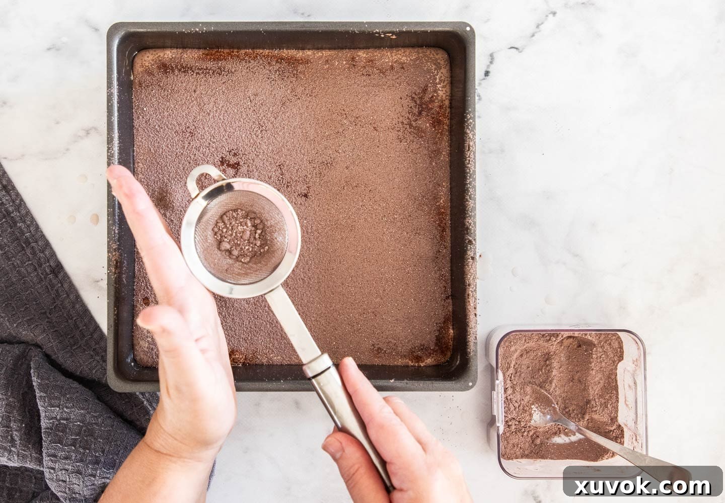 A sifter dusting a mixture of cocoa and icing sugar over the chocolate marshmallow in the pan.