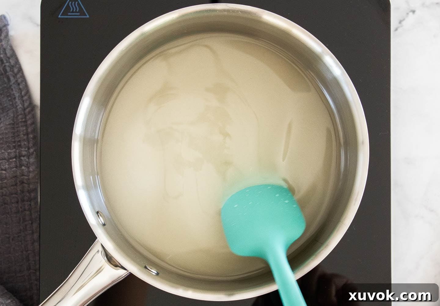 Sugar being stirred into water in a saucepan over medium heat, beginning the syrup making process.